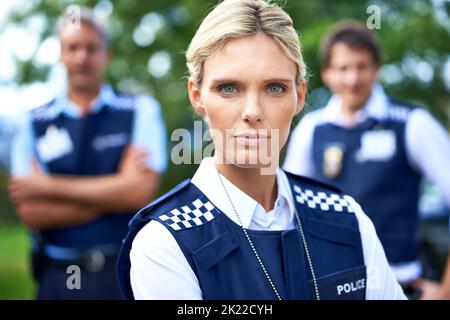 Shes auf Ihren Fall. Eine ernsthafte Polizistin mit ihren Kollegen im Hintergrund. Stockfoto