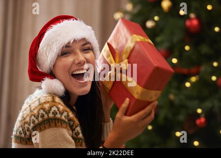 OOH, ich weiß, was es ist. Eine attraktive junge Frau, die versucht, herauszufinden, welches Geschenk sie am Weihnachtsmorgen erhalten hat. Stockfoto