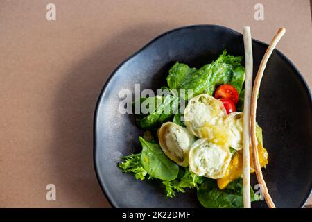 Frühstück am Morgen, cremiges Omelette und Buratta Chesese, Salat Avocado und grüne Blätter auf schwarzem Teller.Essen gesundes Konzept.Salat mit Tomaten Stockfoto