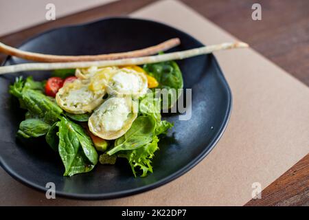 Frühstück am Morgen, cremiges Omelette und Buratta Chesese, Salat Avocado und grüne Blätter auf schwarzem Teller.Essen gesundes Konzept.Salat mit Tomaten Stockfoto