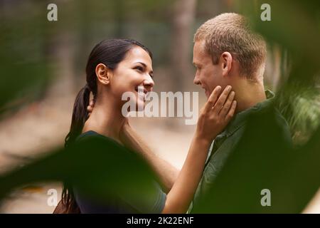 Verloren im Dunst der Romantik im Frühling. Beschnittene Ansicht eines glücklichen jungen Paares, das zusammen im Park steht. Stockfoto