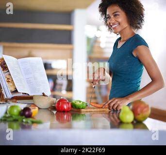 Ein köstliches Gericht von Grund auf. Eine junge Frau, die aus einem Rezeptbuch kocht. Stockfoto