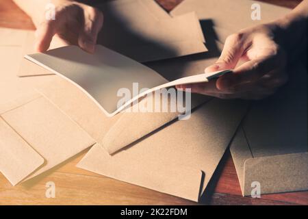Nahaufnahme von schönen Männerhänden, die ein leeres weißes Buch auf dem braunen Holztafel-Hintergrund öffnen. Stockfoto