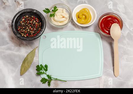Porzellan- und Glasschüsseln mit Ketchup, Senf, Käsesoße und einer Steinschale mit Gewürzen auf dem Küchentisch. Draufsicht. Stockfoto