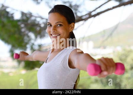 Ich bin damit beschäftigt, stärker zu werden. Porträt einer schönen Frau, die Hanteln an einem Fenster hebt. Stockfoto