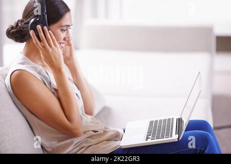 In Kontakt bleiben im digitalen Zeitalter. Eine junge Frau auf einem Sofa, Kopfhörer und einen Laptop. Stockfoto