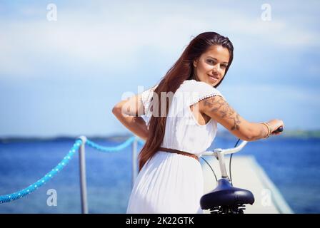 Eine wunderschöne tätowierte junge Frau, die ihr Fahrrad an einem Pier entlang schiebt. Stockfoto