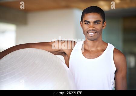 Es gibt mir ein Ganzkörpertraining. Porträt eines jungen Mannes, der einen schweizer Ball hält. Stockfoto