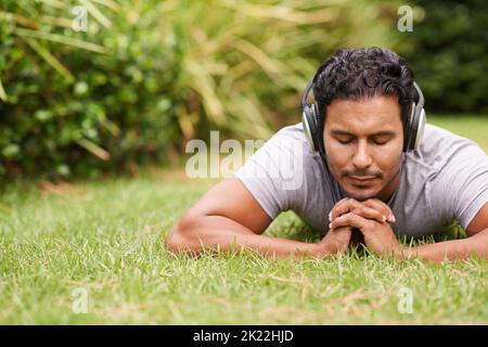 Keine Sorge...ein junger Mann, der auf einem Gras liegt und Kopfhörer trägt. Stockfoto