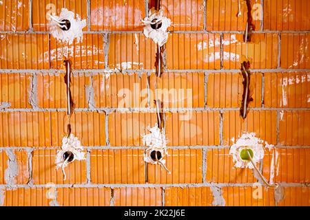 Eine freiliegende Steckdose mit entfernter oberer Abdeckung für die Installation der Verkabelung an der Wand mit im Bau befindlichen Gebäudeblöcken. Stockfoto