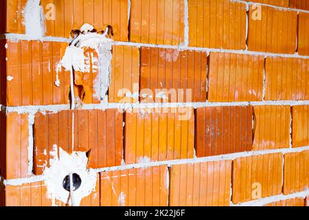 Eine freiliegende Steckdose mit entfernter oberer Abdeckung für die Installation der Verkabelung an der Wand mit im Bau befindlichen Gebäudeblöcken. Stockfoto