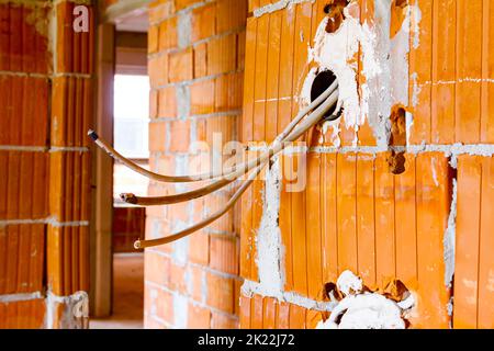 Eine freiliegende Steckdose mit entfernter oberer Abdeckung für die Installation der Verkabelung an der Wand mit im Bau befindlichen Gebäudeblöcken. Stockfoto