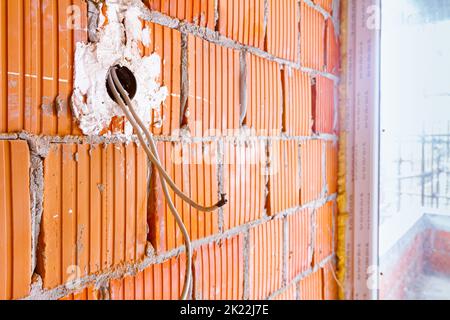 Eine freiliegende Steckdose mit entfernter oberer Abdeckung für die Installation der Verkabelung an der Wand mit im Bau befindlichen Gebäudeblöcken. Stockfoto