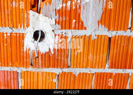 Eine freiliegende Steckdose mit entfernter oberer Abdeckung für die Installation der Verkabelung an der Wand mit im Bau befindlichen Gebäudeblöcken. Stockfoto