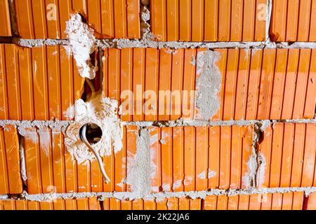 Eine freiliegende Steckdose mit entfernter oberer Abdeckung für die Installation der Verkabelung an der Wand mit im Bau befindlichen Gebäudeblöcken. Stockfoto