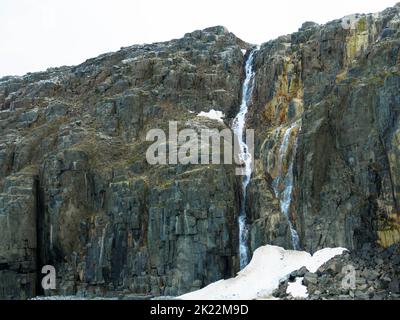 Spektakuläre Aussicht auf einen Wasserfall auf einem Gletscher. Die Vogelklippe Alkefjellet ist die berühmteste Klippe des Spitzbergen-Archipels. Hinloopen Fjord, Spitzbergen. Stockfoto