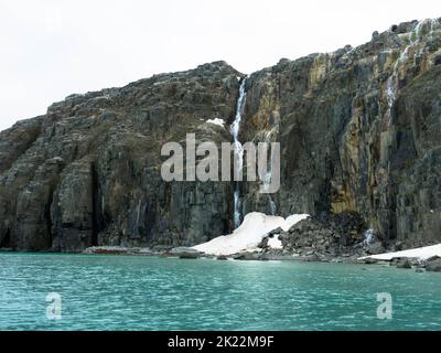 Spektakuläre Aussicht auf einen Wasserfall auf einem Gletscher. Die Vogelklippe Alkefjellet ist die berühmteste Klippe des Spitzbergen-Archipels. Hinloopen Fjord, Spitzbergen. Stockfoto