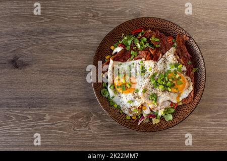 Schmackhaftes, appetitliches Spiegelei, Rührei, mit Fleisch und Speck mit grünem Lebensmittelgeschäft und Mais auf dem Teller auf Holztisch Stockfoto