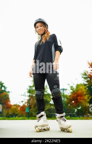 Junge aktive Frau in Rollerklingen mit Helm Stockfoto