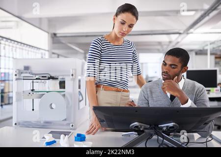 Arbeiten mit modernster Technologie. Zwei Kollegen sprechen über einen Touchscreen-Computer, während sie mit einem 3D-Drucker arbeiten. Stockfoto