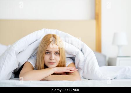 Fauler Sonntag. Guten Morgen. Wochenend-Erholung. Neuer Tag. Entspannte ruhige junge hübsche Frau unter der Decke in weichen sauberen weißen Bettlaken in gemütlichen hellen Schlafzimmer f Stockfoto