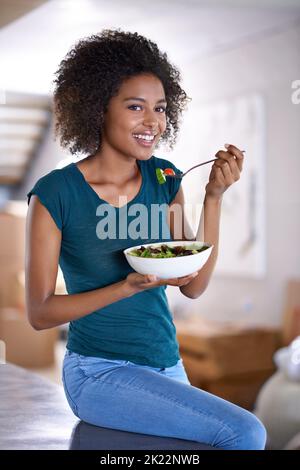 Shes lieben ihre neue Ernährung. Eine schöne junge Frau, die zu Hause eine Schüssel Salat isst. Stockfoto