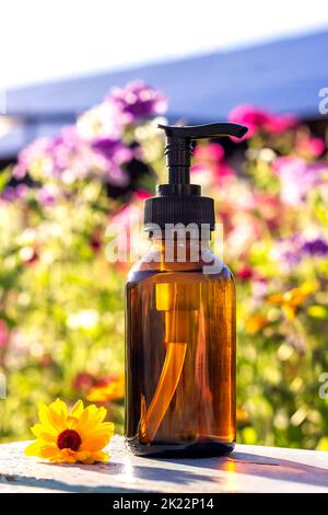 Braune Glasflasche mit Pumpe von Kosmetikprodukten auf hellem floralem Hintergrund. Natural Organic Spa Kosmetik Beauty Konzept Mockup Vorderansicht. Stockfoto