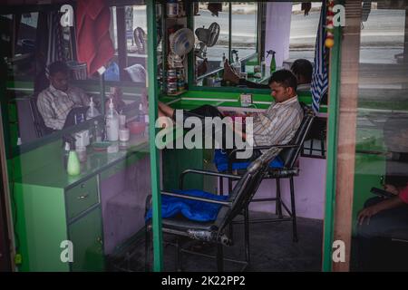 Ein Barbier, der sich ausruhte und sein Telefon mit den Füßen auf dem Tresen in Kathmandu, Nepal, ansah Stockfoto