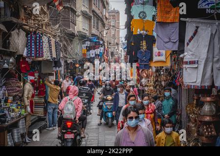 Eine geschäftige Straße eines Marktes in Nepal, Kathmandu, wo Menschen mit Gesichtsmasken und Motorroller vorbeifahren Stockfoto