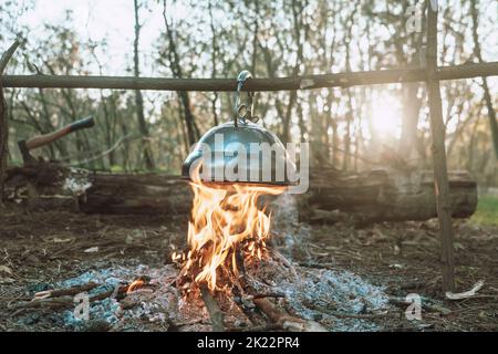 Der Wasserkocher wird an einem hellen Lagerfeuer erhitzt. Wunderbarer Abend atmosphärischen Hintergrund des Lagerfeuers. Reisen Sie im Wald. Stockfoto