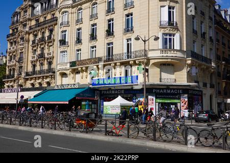 Menschen, Fahrräder, ein geschäftiges Viertel gegenüber einem Pariser Bahnhof mit Apotheke, wo Covid-Tests angeboten werden, und andere Geschäfte im Haussmann-Gebäude. Stockfoto