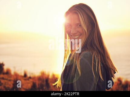 Abenteuer erwartet Sie. Porträt einer Frau, die bei Sonnenuntergang auf einem Hügel steht. Stockfoto