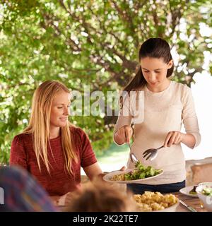 Gibt Mama ein wenig mehr. Eine Frau und ihre Tochter genießen ein Familienessen im Freien. Stockfoto