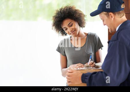 Einfach hier unterschreiben und alles ist Ihr. Ein Kurier, der eine Lieferung an einen lächelnden Kunden macht. Stockfoto