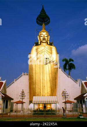 Thailand: Riesiger stehender Buddha, Wat Intharawihan, Bangkok. Das Hauptmerkmal von Bangkoks Wat Intharawihan ist der 32 Meter hohe stehende Buddha, der entweder Luang Pho To oder Phrasiariyametri genannt wird. Die Fertigstellung dauerte über 60 Jahre und ist mit Glasmosaiken und 24-Karat-Gold verziert. Der Knoten des Buddha-Bildes enthält eine Reliquie von Lord Buddha, die aus Sri Lanka gebracht wurde. Der Tempel wurde zu Beginn der Ayutthaya-Zeit erbaut. Stockfoto