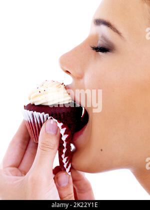 Himmel aus rotem Samt. Studioaufnahme einer schönen jungen Frau, die einen roten Samtkuchen genießt. Stockfoto