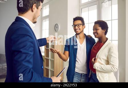 Während des Treffens mit glücklichen jungen verheirateten Paar realtor gibt ihnen Schlüssel zu ihrem neuen Zuhause. Stockfoto