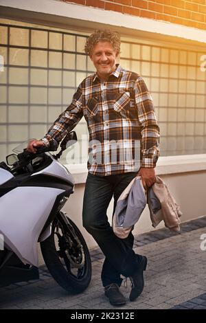 Wie mein neuer Satz von Rädern. Porträt eines glücklichen, reifen Mannes, der sich an sein Motorrad lehnt. Stockfoto