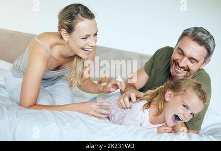 Glückliche Familie, Bett und Spaß Familie spielen und lachen, während mit kleinen Mädchen in einem Schlafzimmer entspannen. Glückliche, verspielte und liebevolle Eltern, die albern damit sind Stockfoto