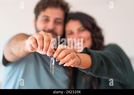 Das junge glückliche Paar, das die Schlüssel aus ihrer neuen Wohnung hält, konzentriert sich auf die Schlüssel, verschwommene Gesichter - Liebe, Familie, Lifestyle-Konzept für Immobilien Stockfoto