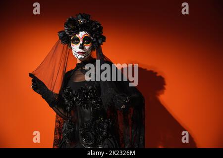 Frau in halloween catrina Make-up berühren schwarzen Schleier auf rotem Hintergrund, Stockbild Stockfoto