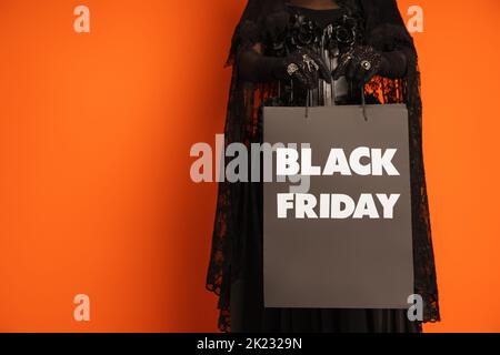 Beschnittene Ansicht der Frau in gruseligen halloween Make-up hält Einkaufstasche mit schwarzem freitag Schriftzug isoliert auf orange, Stock Bild Stockfoto