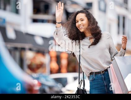 Eine Stadtfrau, die nach einem positiven Einkaufsbummel in einer geschäftigen Stadt ein Taxi und Einkaufstaschen anrief. Junges Mädchen auf der Straße mit Geschäft kaufen Pakete, während Stockfoto