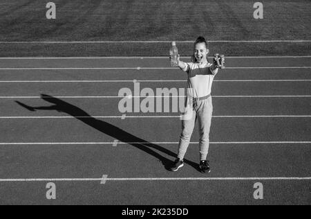 Teenager-Mädchen mit Langhanteln und Wasserflasche. Fitness-Trainer bereiten für das Training. Aufwärmen auf Stadion-Fitnessraum. Kraft und Kraft. Kindertraining bei Stockfoto