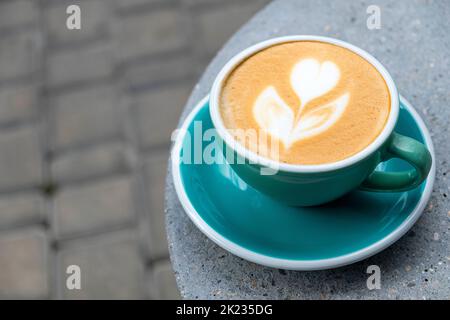 Frisch servierte Tasse Cappuccino mit Latte Art auf einem Holztisch in einem Café. Eine schöne Tasse Cappuccino in Minzfarbe. Stockfoto