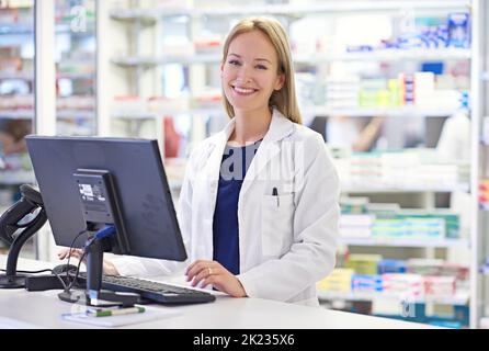 Wie kann ich heute helfen? Porträt eines attraktiven Apothekers am Computer. Stockfoto