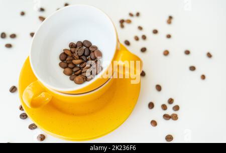Schöner Morgen, der Prozess der Herstellung von Kaffee, eine gelbe Tasse auf einem weißen Tisch, verstreute Kaffeebohnen Stockfoto