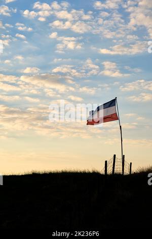 Holländische rot-weiße und blaue umgekehrte Flagge auf einem Deich bei Sonnenuntergang in den Niederlanden. Bauern in den Niederlanden protestieren. Stockfoto