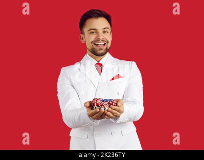 Porträt eines glücklichen Mannes, der auf rotem Hintergrund in seinen Händen Pokerchips hält. Stockfoto