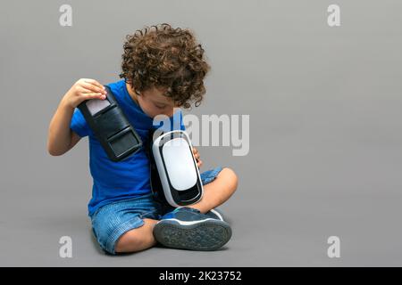 Kind mit einer Virtual-Reality-Brille in den Händen, das neugierig auf ihre Arbeitsweise schaut Stockfoto